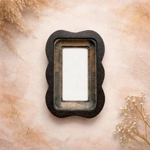 May include: A rectangular picture frame with a dark brown, scalloped wooden outer edge and a lighter brown, recessed inner border. The frame features a smooth, matte finish and surrounds a plain, white, rectangular center space for a photograph.