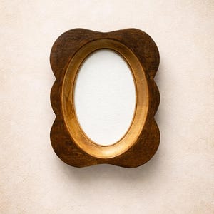 Könnte beinhalten: Ovaler Holzbilderrahmen mit dunkelbrauner Außenseite und goldfarbenem Innenraum. Der Rahmen hat einen gewellten Rand und einen weißen ovalen Platz für ein Foto oder Kunstwerk.