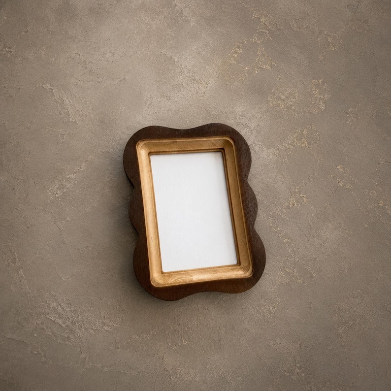 May include: A rectangular picture frame with a dark brown, scalloped outer edge and a smooth, light gold inner border. The frame features a vertical orientation and contains a plain white rectangular insert in the center for displaying a photograph.