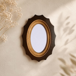 May include: An oval picture frame featuring a dark brown, scalloped outer edge and a smooth, light gold inner border. The frame surrounds a plain white centre area, presenting a high-contrast design with distinct geometric shapes and colours.