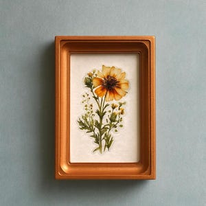 Puede incluir: Una impresión botánica enmarcada que presenta una ilustración detallada de una flor amarilla y marrón con follaje verde. La obra de arte está enmarcada en un marco rectangular dorado, creando una estética clásica. El fondo es azul claro liso.