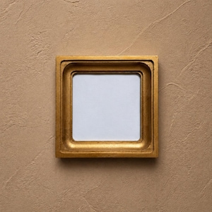May include: A square picture frame with a metallic gold finish and a stepped, recessed inner border. The frame features a smooth, reflective surface and contains a plain, white, square-shaped centre insert for displaying artwork or photographs.