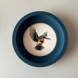 May include: A blue circular frame with a white background and a painting of a blue and brown kingfisher in flight.