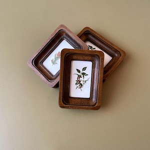 May include: Three small, vintage wooden picture frames with botanical prints. The frames are a warm brown color and have a layered design. The prints feature detailed illustrations of plants and flowers.