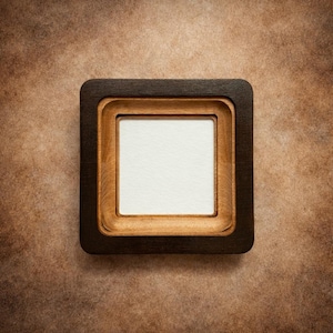 May include: Square wooden picture frame with a dark brown outer frame and a lighter brown inner frame. The center features a white square, likely for a photo or artwork. The frame is set against a textured brown background.