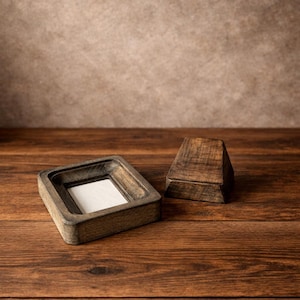 Puede incluir: Dos cajas de madera sobre una superficie de madera. Una caja es cuadrada con un interior empotrado y un inserto blanco. La otra caja es un peque&ntilde;o prisma triangular. El fondo es una pared texturizada neutra.