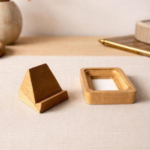 May include: Two wooden desk accessories: a triangular phone stand and a rectangular tray. Both are made of light-colored wood and sit on a neutral-toned surface. The phone stand is angled for optimal viewing.