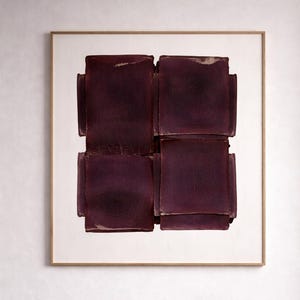 May include: Abstract art print featuring a square composition of dark purple, textured shapes. The artwork is framed in a gold-colored frame and hangs above a wooden chair with a woven cane seat and back. The chair is set on a dark wood floor.