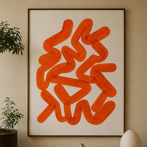 Op de afbeelding: Een abstracte kunstprint met heldere oranje penseelstreken op een witte achtergrond, omlijst in donker hout. Het kunstwerk hangt boven een houten bank met boeken, een vaas en een bolvormige lamp. Links staat een boom in een pot.