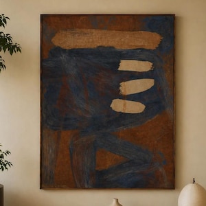Op de afbeelding: Abstract kunstwerk in een houten lijst. Het stuk heeft een bruine achtergrond met blauwe penseelstreken en drie beige horizontale vormen. Het hangt boven een houten bank met boeken, een vaas en een lamp.