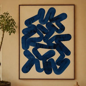 Op de afbeelding: Abstracte kunstprint met gedurfde, blauwe penseelstreken op een crèmekleurige achtergrond, omlijst in donker hout. Een kleine boom in een houten plantenbak en een rustieke houten bank met boeken en een sculptuur maken het interieur compleet.