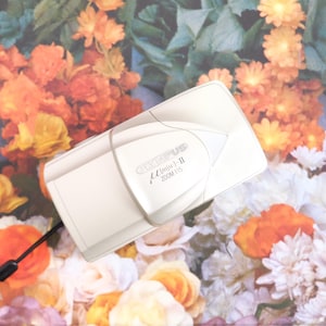 May include: A champagne-coloured Olympus mju: II Zoom 115 compact film camera with a sliding lens cover. The camera features a black wrist strap attached to the side and the brand name and model text printed clearly on the front casing.