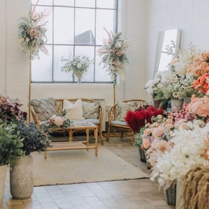 May include: A floral shop interior with a white brick wall, a large window, and a wicker sofa with pillows. There are many bouquets of flowers in various colors and styles, including pink, white, and red.