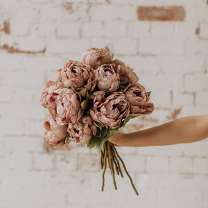 May include: A bouquet of blush pink peonies with green stems.