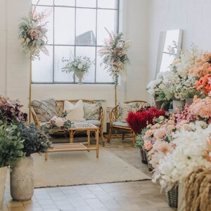 May include: A floral shop interior with a white brick wall, a large window, and a wicker sofa with pillows. There are many bouquets of flowers in various colors and styles, including white, pink, red, and orange.