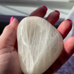 Peut inclure: Un cristal de sélénite blanc en forme de cœur avec des stries visibles. Le cristal est lisse et poli.