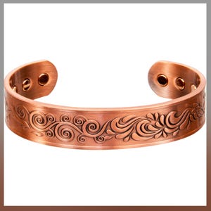 May include: A copper-colored cuff bracelet with an open design. The bracelet features an embossed floral pattern along the front and has a curved shape. The ends of the bracelet have two small, round, dark-colored accents.