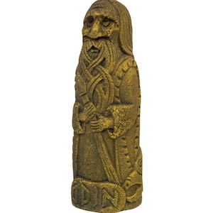 Puede incluir: Una estatua de piedra de color dorado que representa a un hombre barbudo con tallas intrincadas. La estatua est&aacute; de pie y tiene la palabra "ODIN" tallada en la parte inferior.