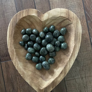 May include: A heart-shaped wooden bowl filled with green and black tumbled stones.