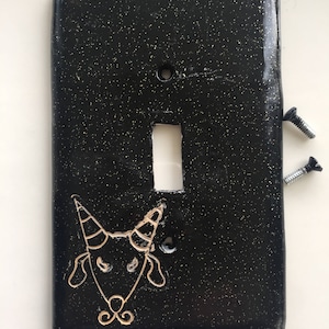 May include: Black light switch cover with gold glitter and a gold unicorn illustration.