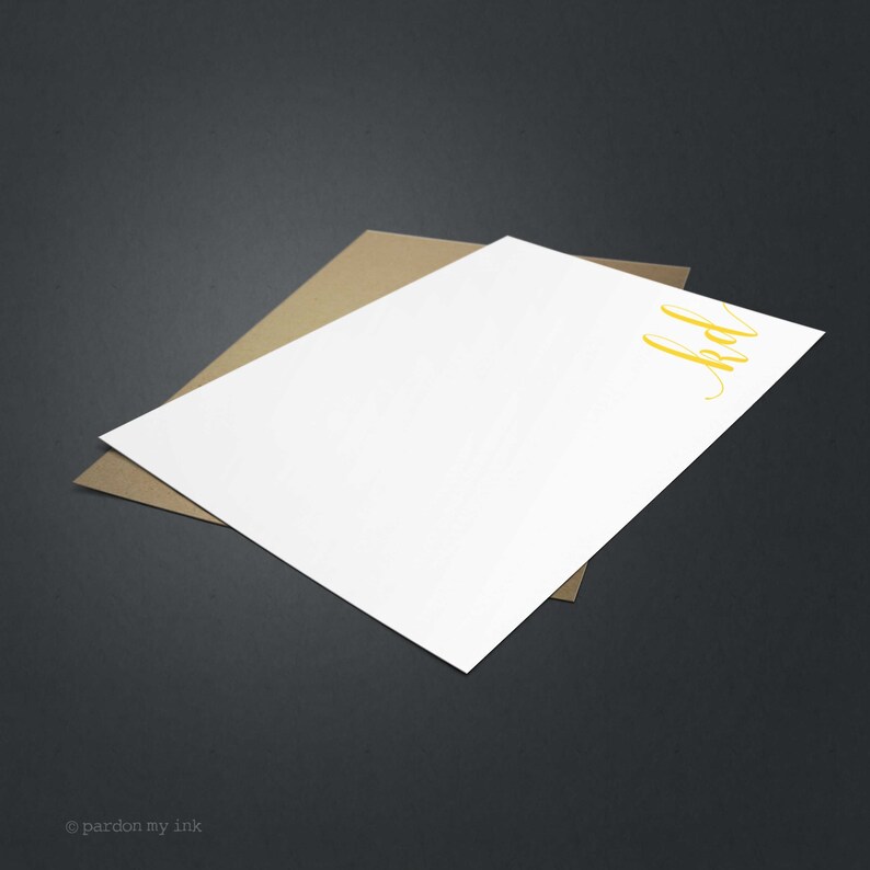 May include: A white stationery card with a yellow handwritten monogram "bd" on the top right corner. The card is on top of a brown envelope.