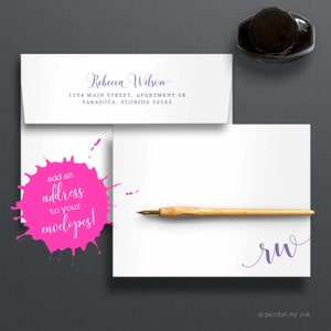 May include: A white envelope with a pink splatter design and the text "add an address to your envelopes!"  The envelope is addressed to Rebecca Wilson at 1234 Main Street, Apartment 6B, Sarasota, Florida 34243.  A wooden calligraphy pen and a black inkwell are also pictured.