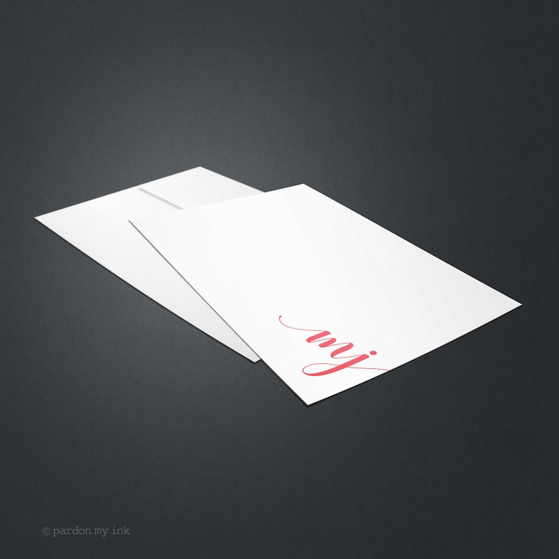 May include: A white card with a red cursive "my" written on it. The card is folded in half and is sitting on a grey surface.