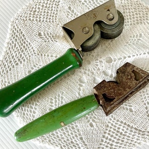 May include: Two vintage kitchen tools with green wooden handles. One is a knife sharpener with two metal wheels and the other is a can opener with a metal blade.