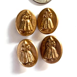 May include: Four oval-shaped gold-toned buttons, each featuring a raised relief design of a person wearing a traditional bonnet and skirt. A United States quarter is positioned above the buttons to provide a sense of scale for the items.