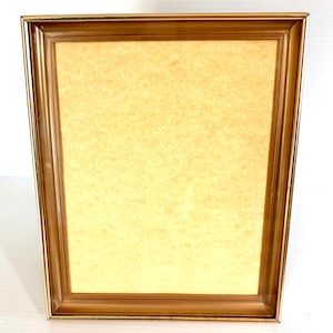 May include: A rectangular, gold-colored picture frame with a light yellow backing. The frame has a simple, classic design with a slightly beveled edge. The frame is empty, ready to display a photograph or artwork.