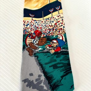 May include: A silk tie with a baseball theme. The tie features a cartoon image of two baseball players in a game. The background is a baseball stadium with a crowd of people. The tie is in shades of green, blue, red, white, and gray.