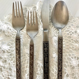 May include: A set of four silver-toned flatware pieces with floral designs on the handles. The set includes a knife, fork, spoon, and a smaller fork.