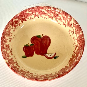 May include: A yellow ceramic bowl with a red rim and a red apple design. The bowl has a speckled glaze.