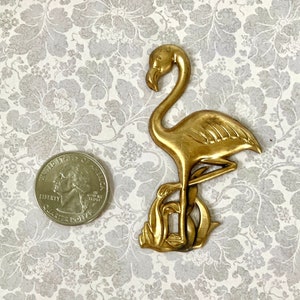 May include: Gold-toned metal flamingo figurine with detailed feathers and a stand. The figurine is about the size of a quarter.