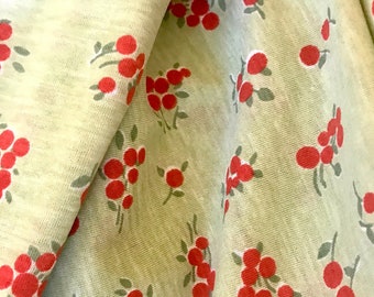 May include: A close-up of a light green fabric with a repeating pattern of red berries and green leaves.