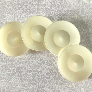 May include: Four ivory-colored ceramic candle holders with a raised center. The candle holders are arranged in a semi-circle.