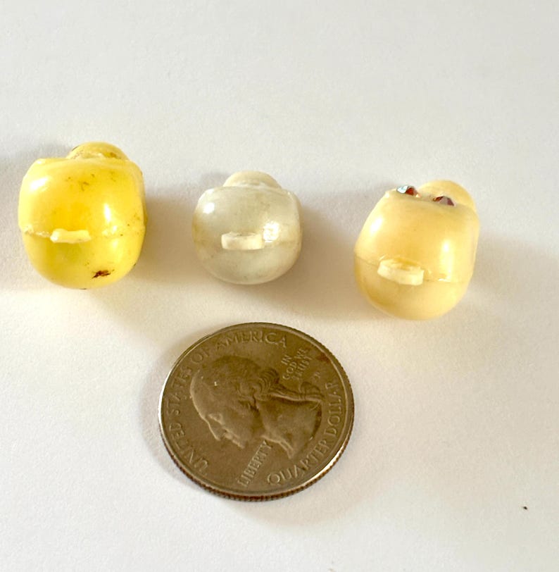 May include: Three small, rounded, smooth plastic buttons with central shanks. One is bright yellow, one is off-white, and one is pale cream with two small embedded red accents. A United States quarter coin is placed below for scale reference.