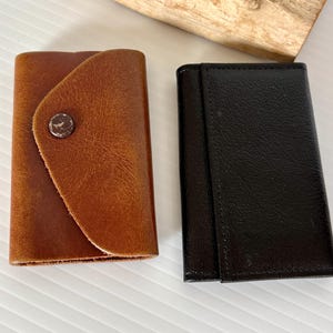 May include: Two leather keychains, one brown and one black. Both keychains have a simple design and are made of high-quality leather.