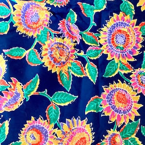 May include: A blue fabric with a repeating pattern of colorful sunflowers. The sunflowers have yellow petals, orange centers, and purple and pink accents. The leaves are green with yellow outlines.