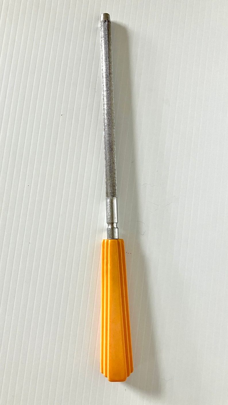 May include: A silver metal file with a yellow plastic handle. The handle has a geometric design.