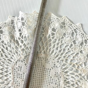 May include: A silver metal file with a textured surface. The file is lying on a white crocheted doily.