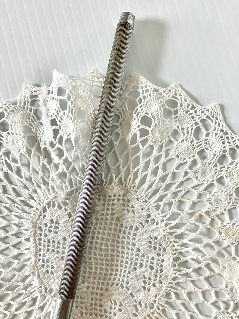 May include: A silver metal file with a textured surface. The file is lying on a white crocheted doily.