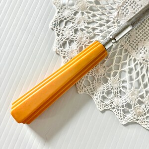 May include: A vintage yellow plastic handled knife with a metal blade. The knife is lying on a white crocheted doily.