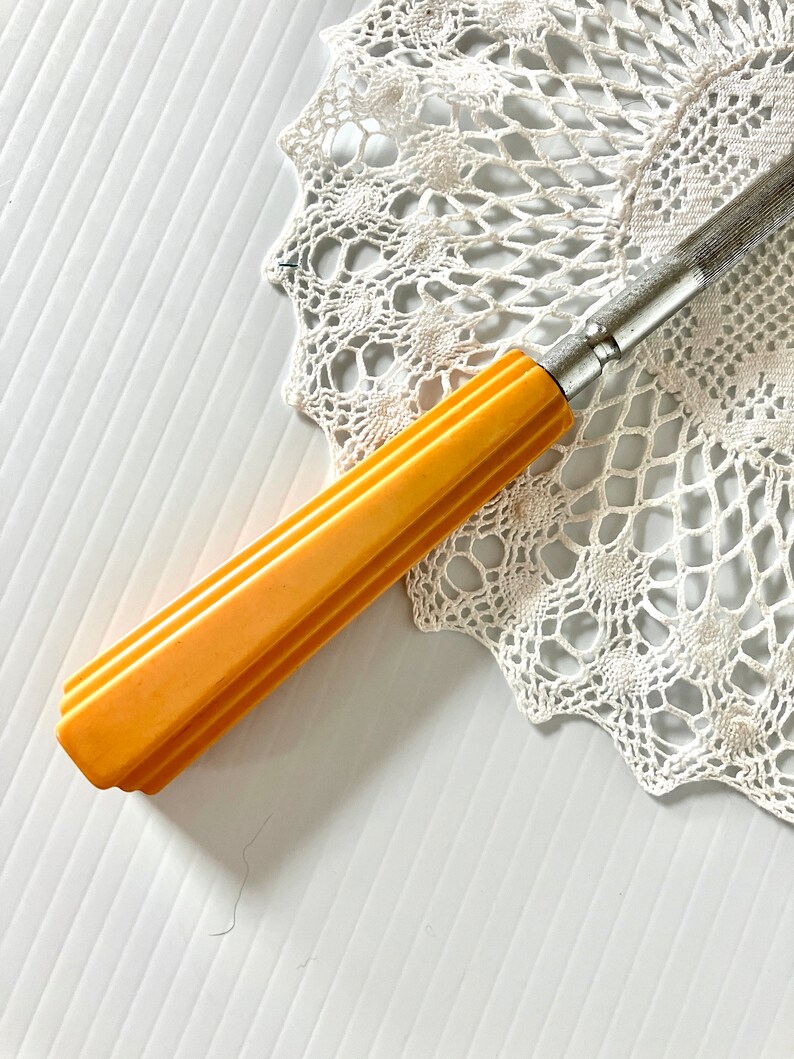 May include: A vintage yellow plastic handled knife with a metal blade. The knife is lying on a white crocheted doily.