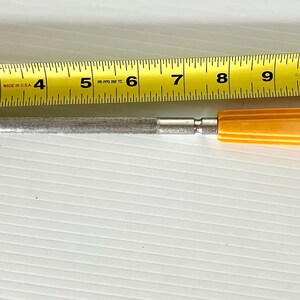 May include: A silver metal knife sharpener with a yellow plastic handle. The sharpener is 11 inches long.