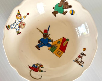 May include: Cream-colored ceramic bowl with a scalloped edge, featuring colorful illustrations of a clown, bears, a dog, and a house. The bowl has a playful, vintage aesthetic, perfect for serving snacks or displaying as decor.