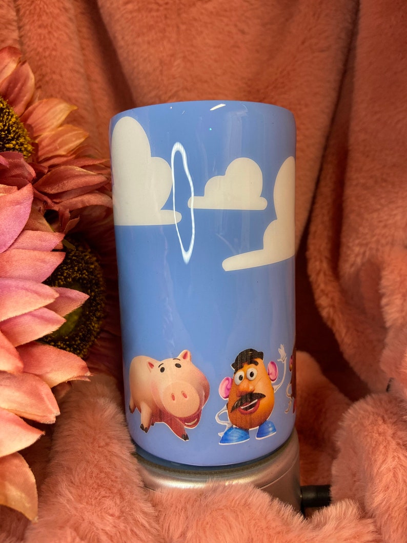 May include: A light blue tumbler with a white cloud design and characters from the Toy Story film. The characters include a pig, a potato head, and a cowboy.