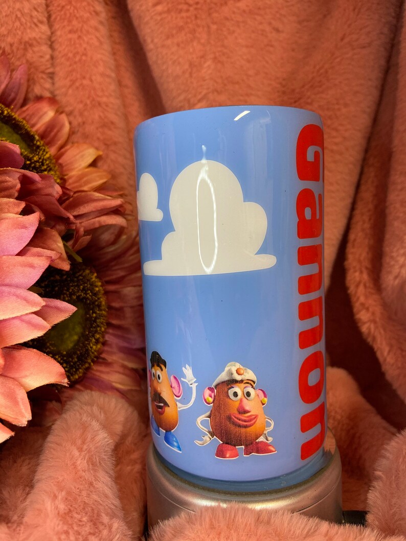 May include: A blue tumbler with a white cloud design and the name "Gannon" in red lettering. The tumbler features a cartoon image of Mr. and Mrs. Potato Head from the Toy Story film.