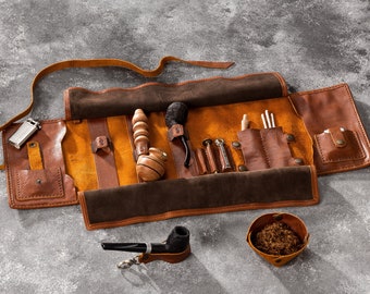 May include: A brown leather tobacco pipe roll with a variety of tools and accessories, including a wooden pipe, a metal pipe, a small bowl, and a lighter. The roll is open and laid flat on a gray surface.