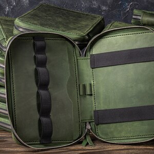 May include: A green leather zipped pouch with multiple compartments and elastic loops for holding pens or other small items. The pouch is open to reveal the interior.